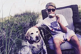 The boy sits in a beach chair eating a popsicle with a yellow lab beside him.