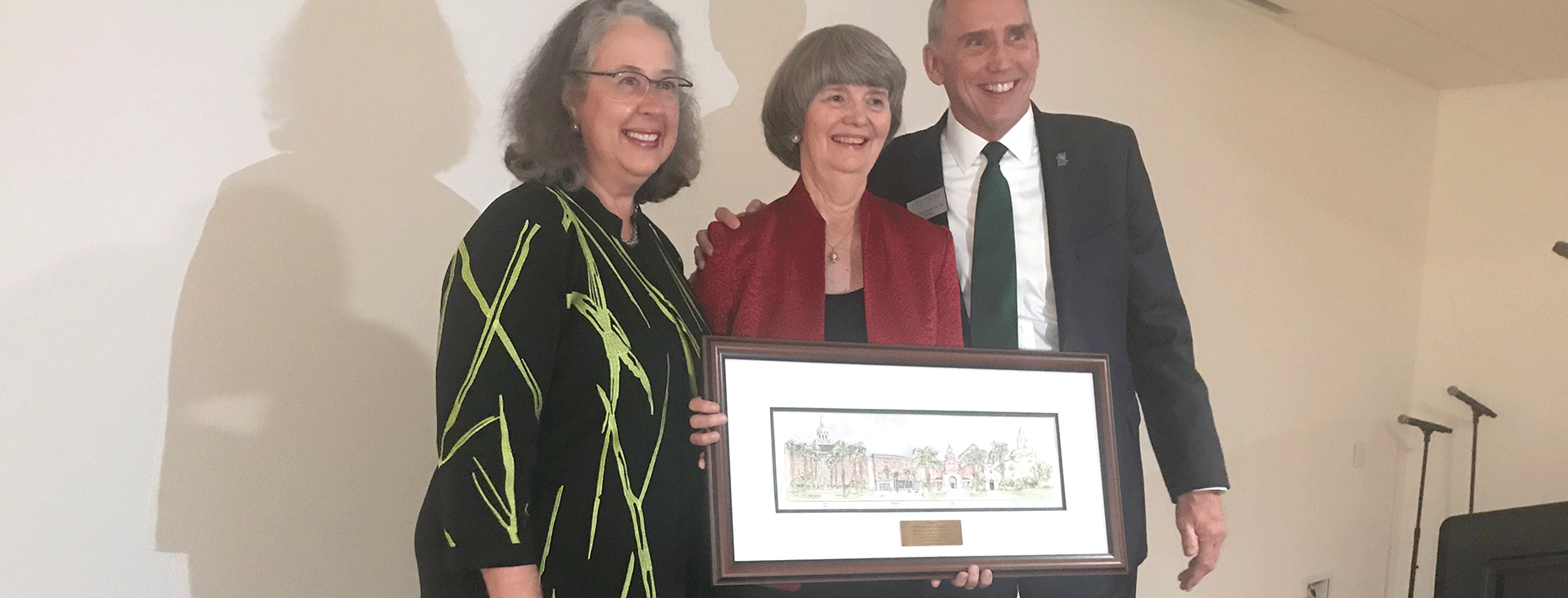 Wendy Libby and Joe Cooper honor Linda Davis, who stands holding a paintiing