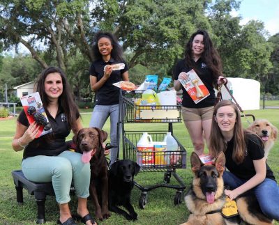 Four students pose with various pet items and service dogs