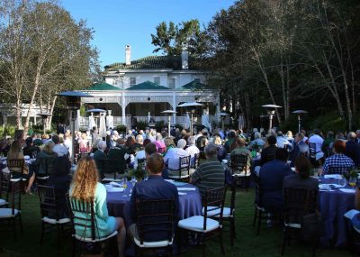 A panoramic of the crowd seated at tables in the garden behind the President's Home