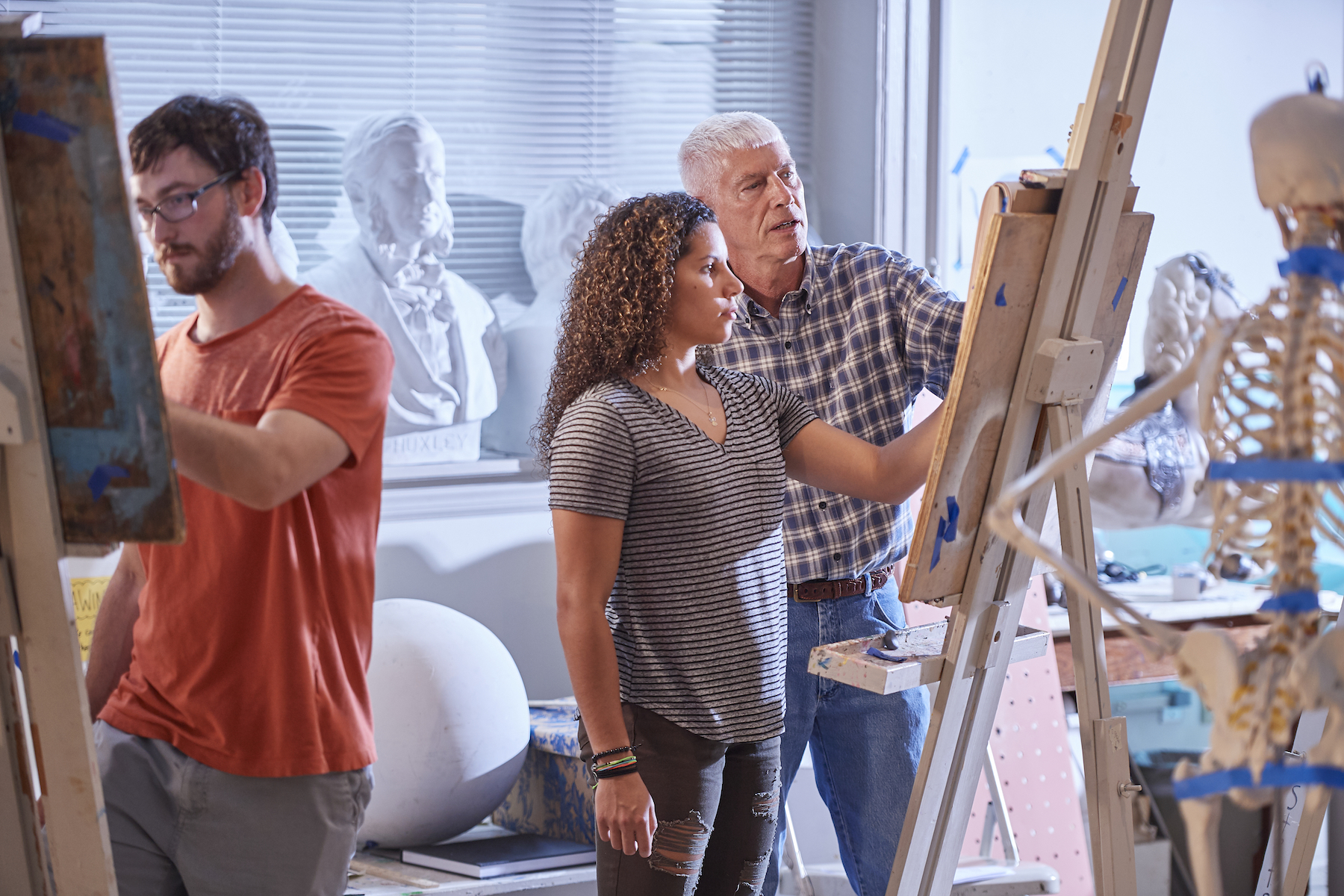 Dan Gunderson stands working with a student at an art easel in a studio classroom at Stetson