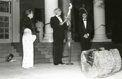 President Edmunds stands with a lighted torch with others watching.