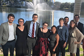 A group shot of all the people along a lakeshore with a fountain in the back.