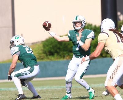 Quarterback is throwing the ball past opposing teammates.