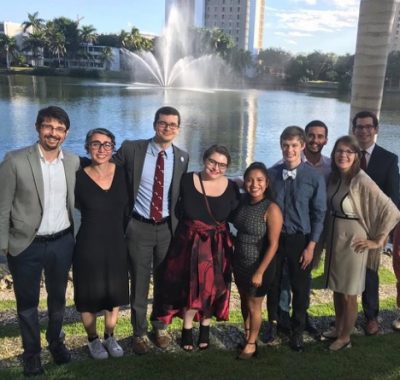 A group shot of all the people along a lakeshore with a fountain in the back.