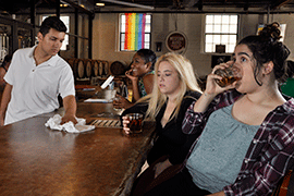 Bartender wipes down bar as three women sit drinking.