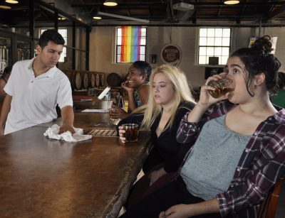 Bartender wipes down bar as three women sit drinking.