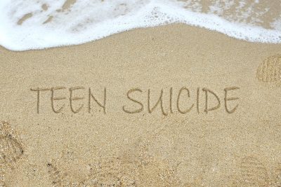 "Teen Suicide" is written in the sand as a bit of wave washes in.