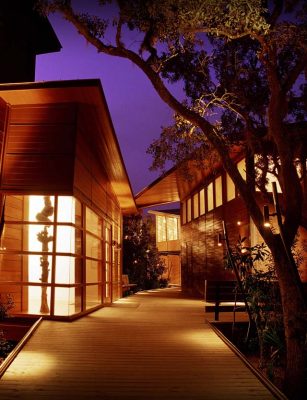 exterior building shot at night with pretty wooden walkways and lights inside the windows.