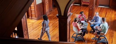 A scenic shot in historic Elizabeth Hall as Dr. Hill sits in a desk, talking to three students.