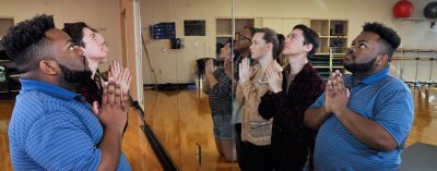 The group is kneeling in front of a large mirror, in praying position, looking toward heaven.