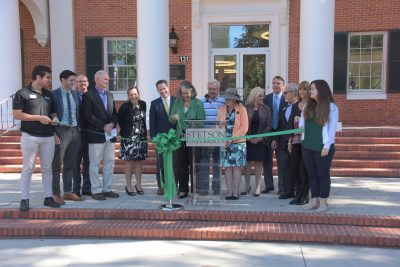 A line of dignitaries watch as Wendy Libby cuts a big green ribbon