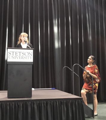 Autumn stands at podium that says Stetson University as the professor stands nearby on the floor.,