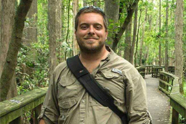 Dustin Angell is walking on an elevated walkway through a forested park.