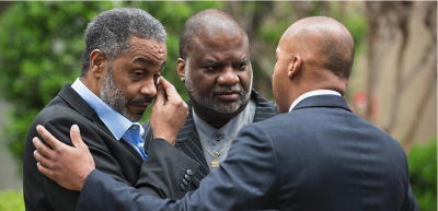 Anthony Ray Hinton wipes away a tear as a friend stands beside him and his attorney touches his shoulder.