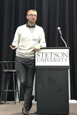 Keynote speaker stands beside the podium, talking