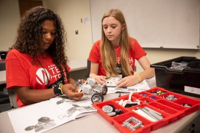 two girls are seated at a table building a robotics rover in a classroom