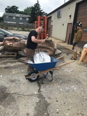 Sculptor has a hammer in hand and is ready to strike mold in a wheelbarrow