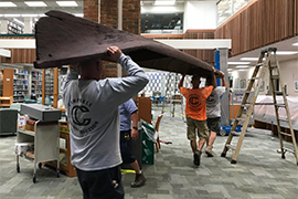 three workers carry an old Native American dugout canoe into the library lobby