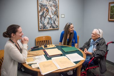 The three women sit around a table with old yellowing documents