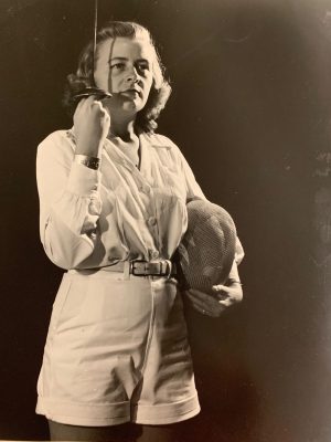 Eloise Newell in black and white photo holds a sword and helmet for fencing