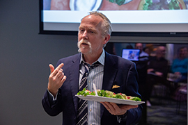 Michael Denner gives lecture and has plate of food in his hand as he talks