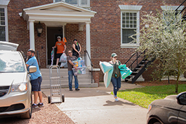 Students walk out of a residence hall carrying their belongings