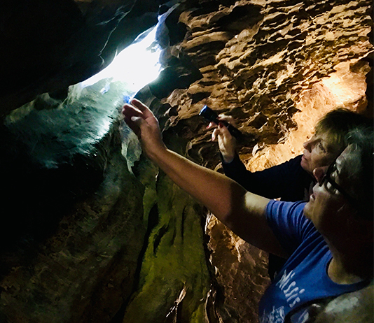 Two women reach toward his signature in a cave