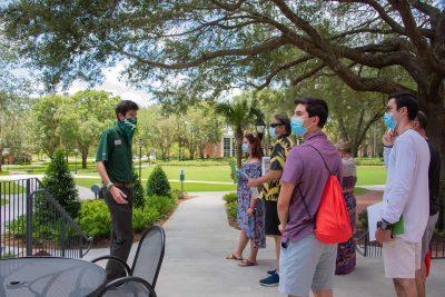 A tour guide leads a small group across campus, all of them wearing face coverings