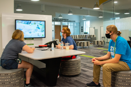 three students play a video game in the CUB's second floor north lobby