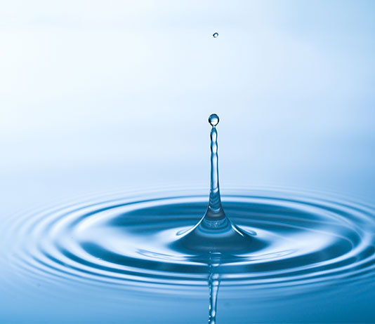 a drop of water breaks the calm surface of water