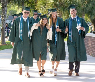 Four students walk to Commencement in their caps and gowns.