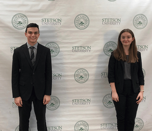 The two students stand in front of a background with Stetson University and its seal.