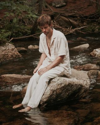 Stephen May sits on a rock in the middle of a stream in a forest.