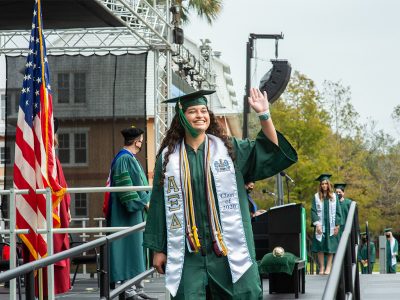A student waves as she walks off the Commencement ceremony stage.