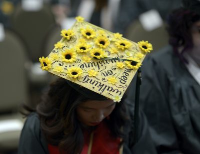 A woman's cap is decorated for Commencement with yellow daisies