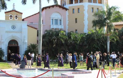 A line of graduates walks across the lawn for graduation.