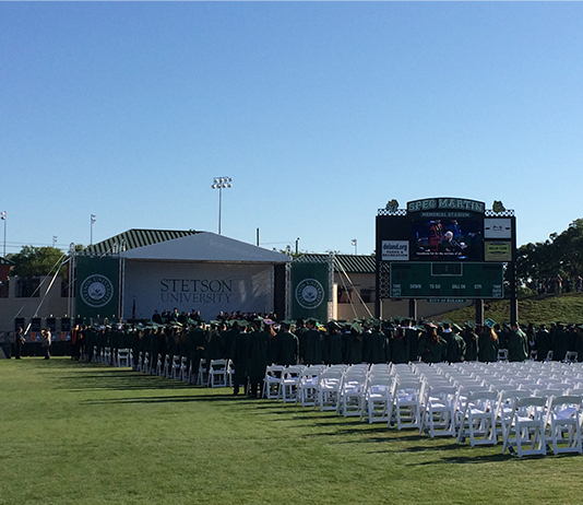 A photo from a distance of graduates and the Commencement stage in the stadium