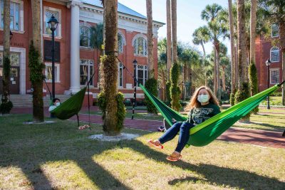 Students relax in hammocks in Palm Court and wear face coverings