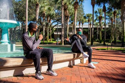 Two students with face coverings share a laugh beside the fountain