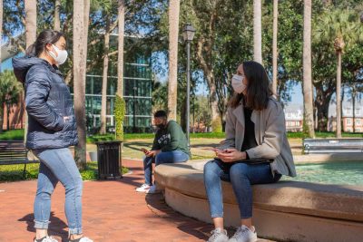 three students sit around Holler Fountain in Palm Court with face coverings