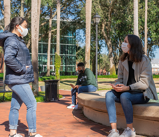 students relax by Holler Fountain in Palm Court with face coverings