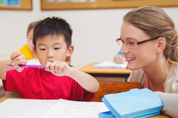 A teacher watches a young student as he works