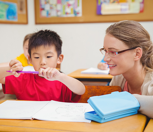 A teacher watches a young student as he works