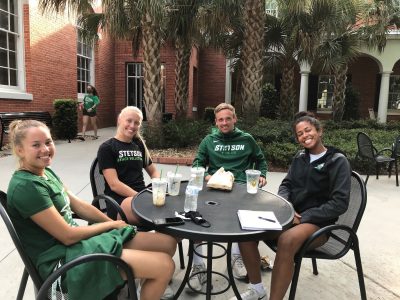 Four student-athletes sit outside the CUB