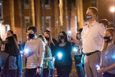 A small crowd of students and President Christopher Roellke hold their cellphones with flashlights on