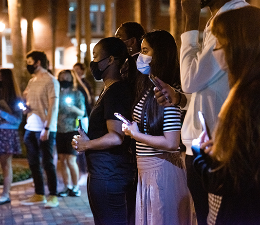 Students stand holding cellphones with the flashlights on