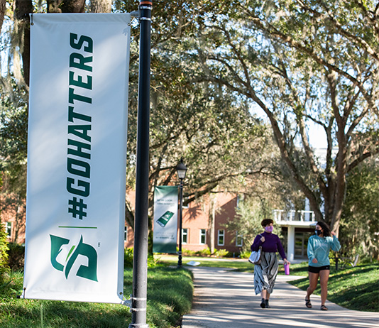 A "Go Hatters" banner hangs on campus as two students in masks walk by