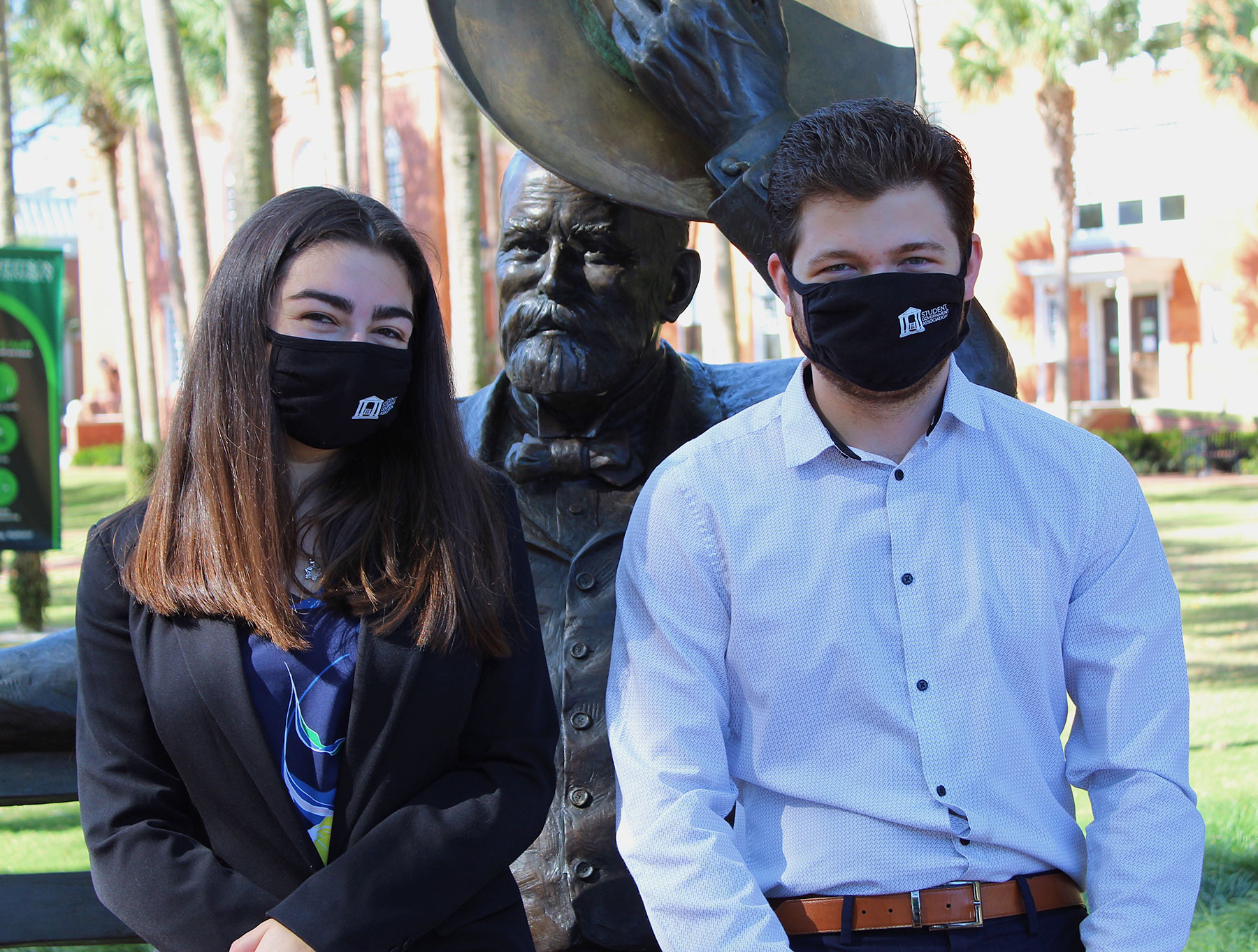 The two SGA officers wear a face covering and sit on the lap of the John B. Stetson statue.
