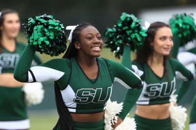 cheerleading squad shakes pom-poms on the sidelines of a game.